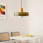 An olive-green glass disc pendant with a frosted globe hangs over a white round table with rattan chairs and lemons, from Clérachic.