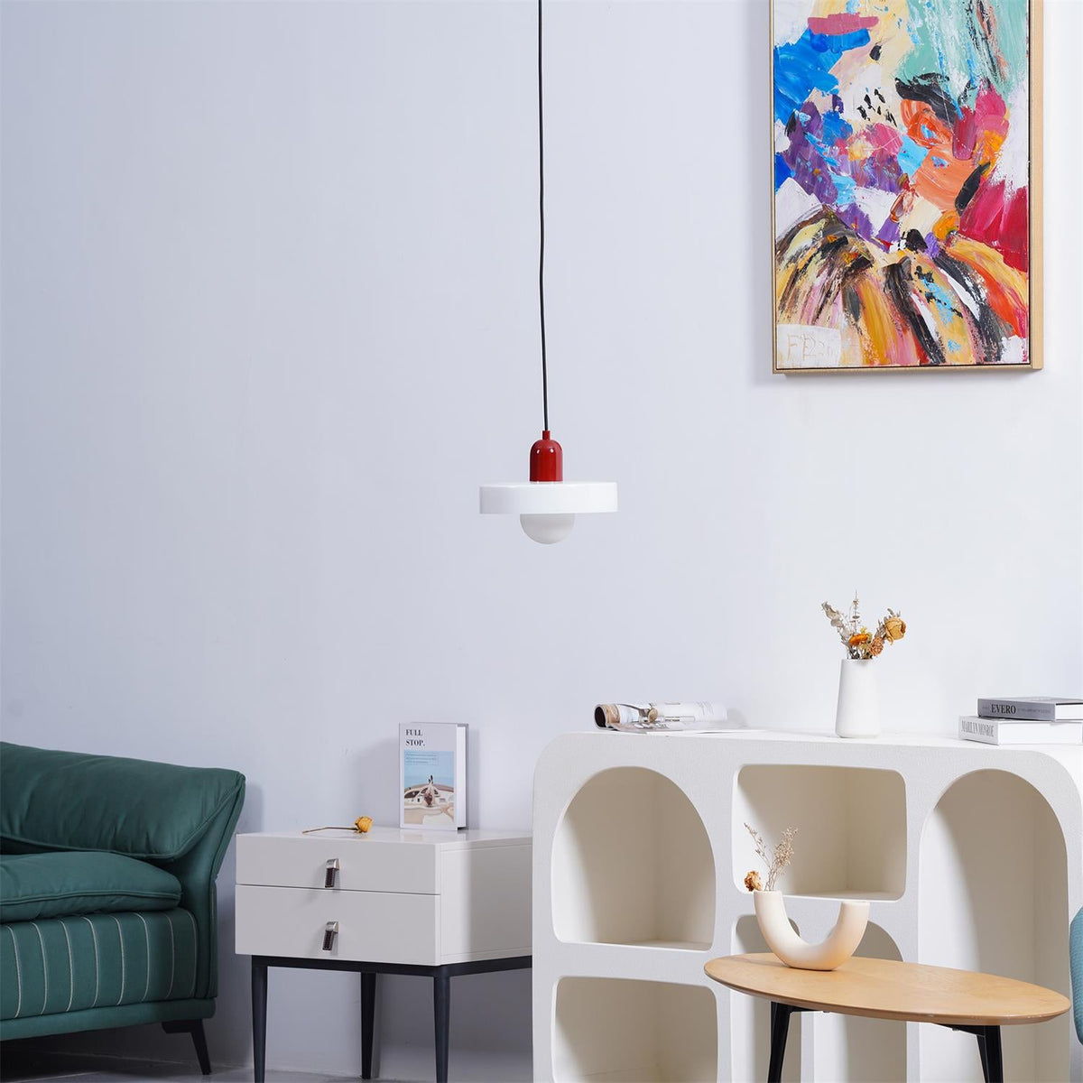 A small white disc pendant with a red cap hangs on a black cord before a bright abstract painting, a Clérachic accent over a living room.