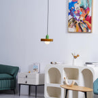 A small olive-green disc pendant with a green cap hangs beside the abstract painting and a teal sofa, a Clérachic accent in a living room.