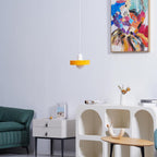 An orange disc pendant with a white cap hangs against a pale wall, below a colourful painting and above a teal sofa, from Clérachic.