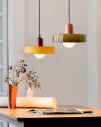 An orange disc with a deep red cap and an olive-green disc with a pink cap hang over a wooden desk by a window, from Clérachic.