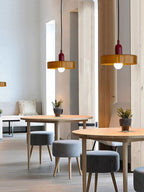 Two orange glass disc pendants hang in a café with round wooden tables and grey upholstered stools, from Clérachic.