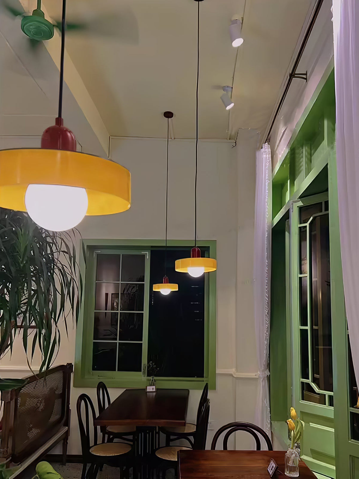 A large orange disc pendant glows in the foreground of a green-framed café with more discs behind it, a Clérachic light at night.