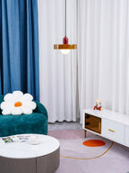 A small orange disc pendant with a red cap hangs in a living room with a teal sofa, a daisy cushion and a white coffee table, from Clérachic.