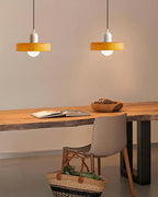 A white-capped disc and a second orange disc glow warm above a live-edge wooden desk and a grey chair, from Clérachic.