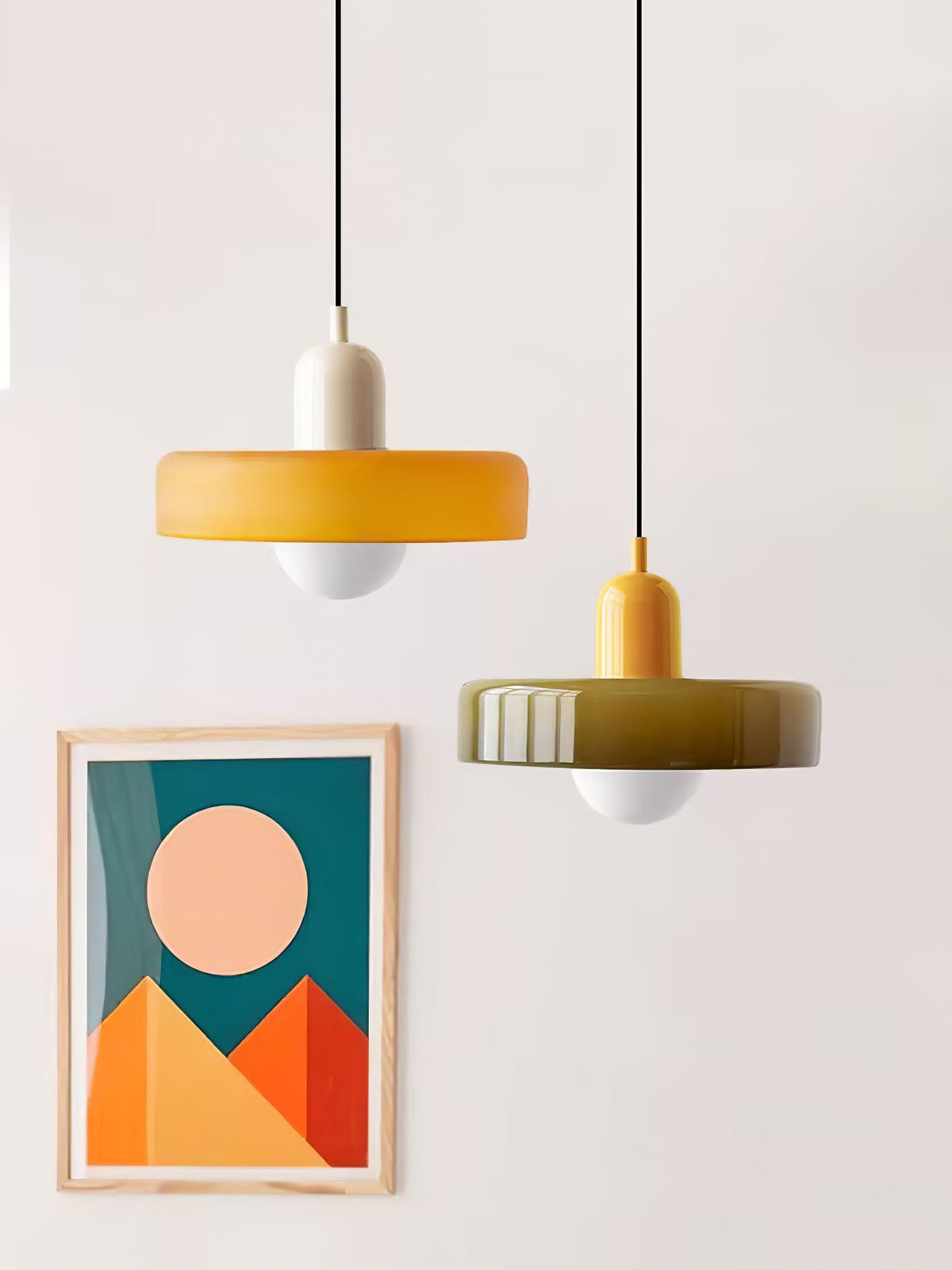 An orange disc with a beige cap and an olive disc with a yellow cap hang beside a geometric mountain print, a Clérachic duo.