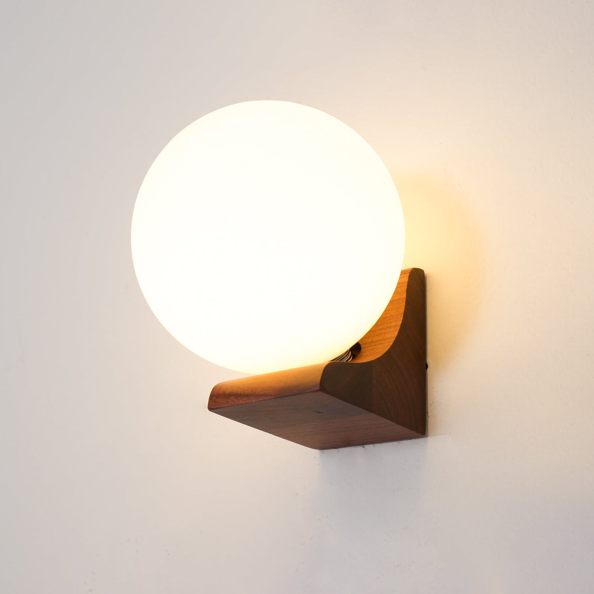 Close view of a glowing white glass globe held by a walnut-toned wooden bracket on a Clérachic wall light.