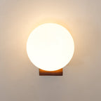 Front view of a warmly lit glass sphere above a short wooden bracket, this Clérachic wall light on a cream wall.