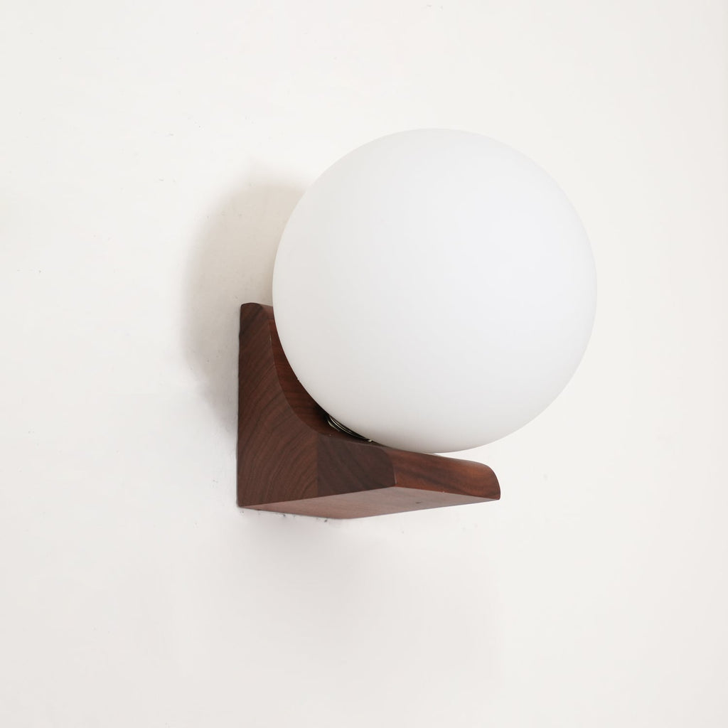 Unlit white glass orb on a dark walnut wooden bracket, this Clérachic wall light mounted on a white wall.