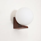 Unlit white glass orb on a dark walnut wooden bracket, this Clérachic wall light mounted on a white wall.