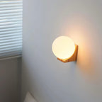This Clérachic orb wall light casts a warm halo on a grey corner wall, its light wooden bracket just below the glass.