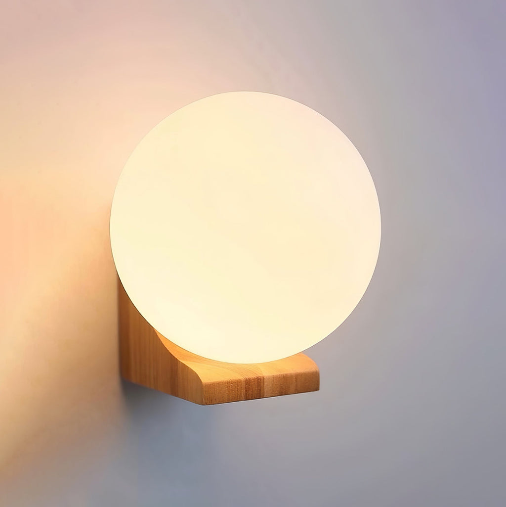 Close view of a lit glass globe on a light wood bracket, this Clérachic wall light against a pinkish wall.