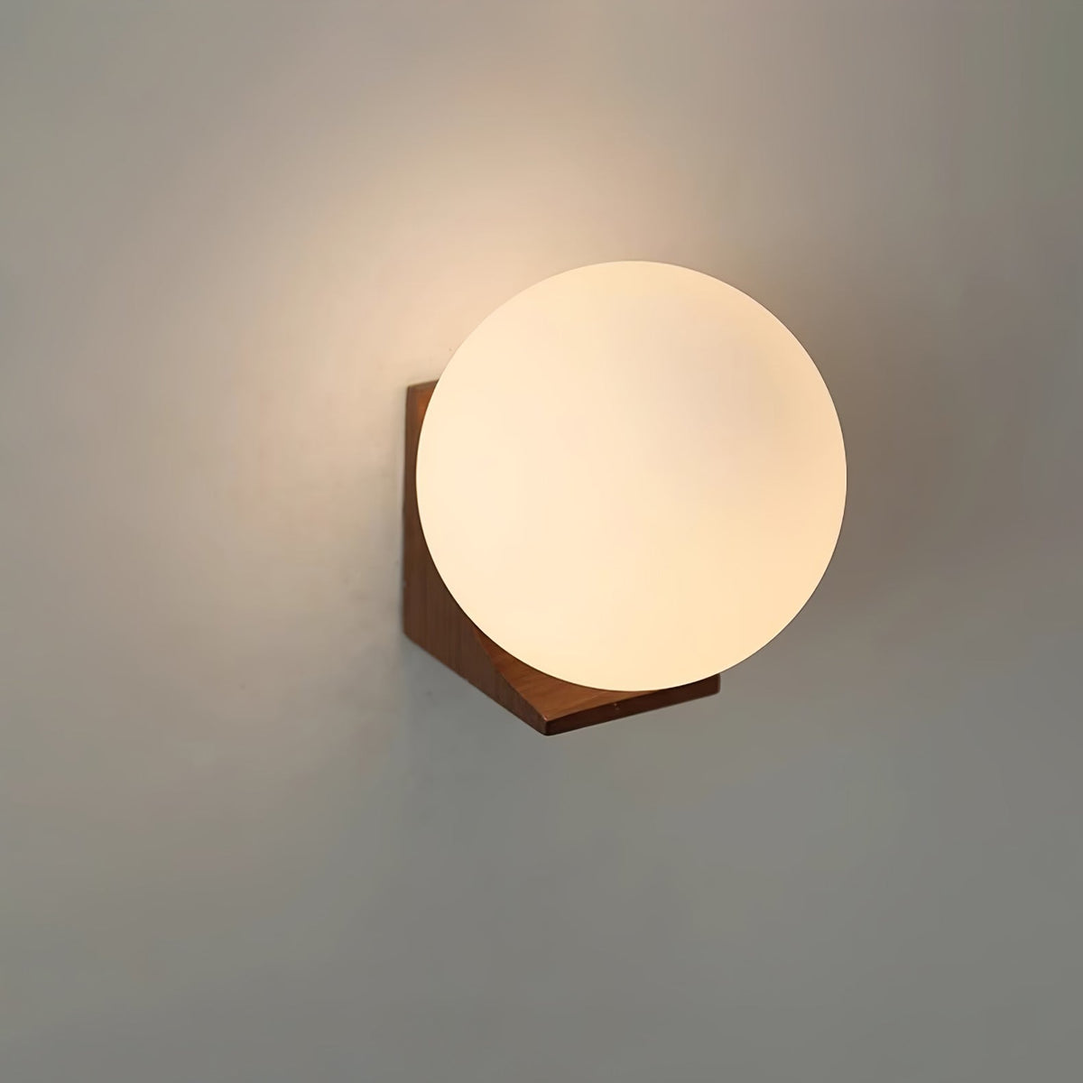 Lit Clérachic glass orb on a light wood bracket, with a warm glow spreading across a grey wall behind it.