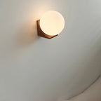 Small Clérachic orb wall light, lit, set high on a grey curved wall with its light wooden bracket beneath the glass.