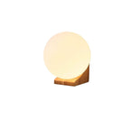 Lit white glass sphere on a small light wood bracket, this Clérachic wall light on a white background.