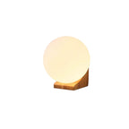 Side view of this Clérachic glass orb wall light on white, with the glowing sphere seated on a pale wooden bracket.