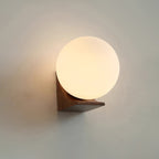 Lit Clérachic orb wall light in a walnut tone, its warm glow fading across a grey-green wall above the dark wood bracket.