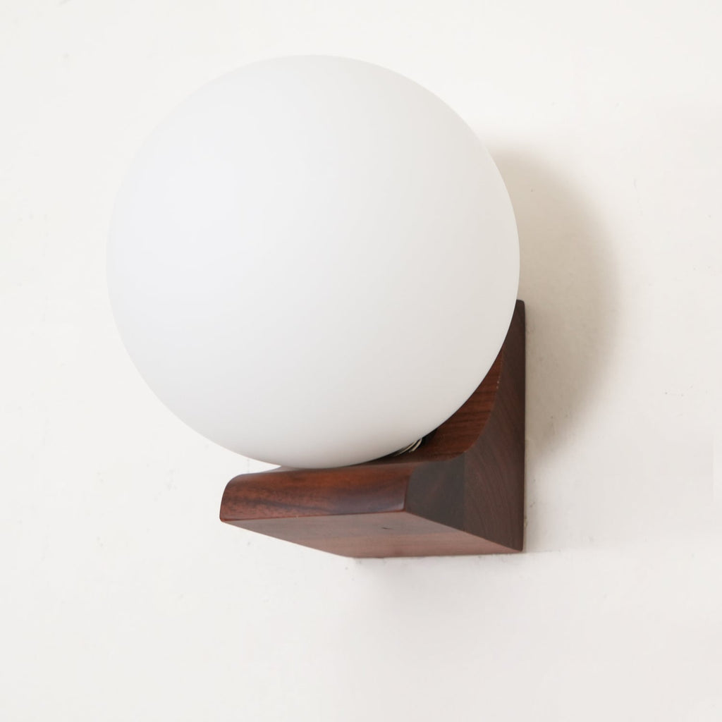 Close view of an unlit frosted glass orb on a dark walnut bracket, this Clérachic wall light against a cream wall.