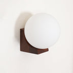 Three-quarter view of this Clérachic wall light, with the frosted glass orb set into a walnut bracket on a cream wall.