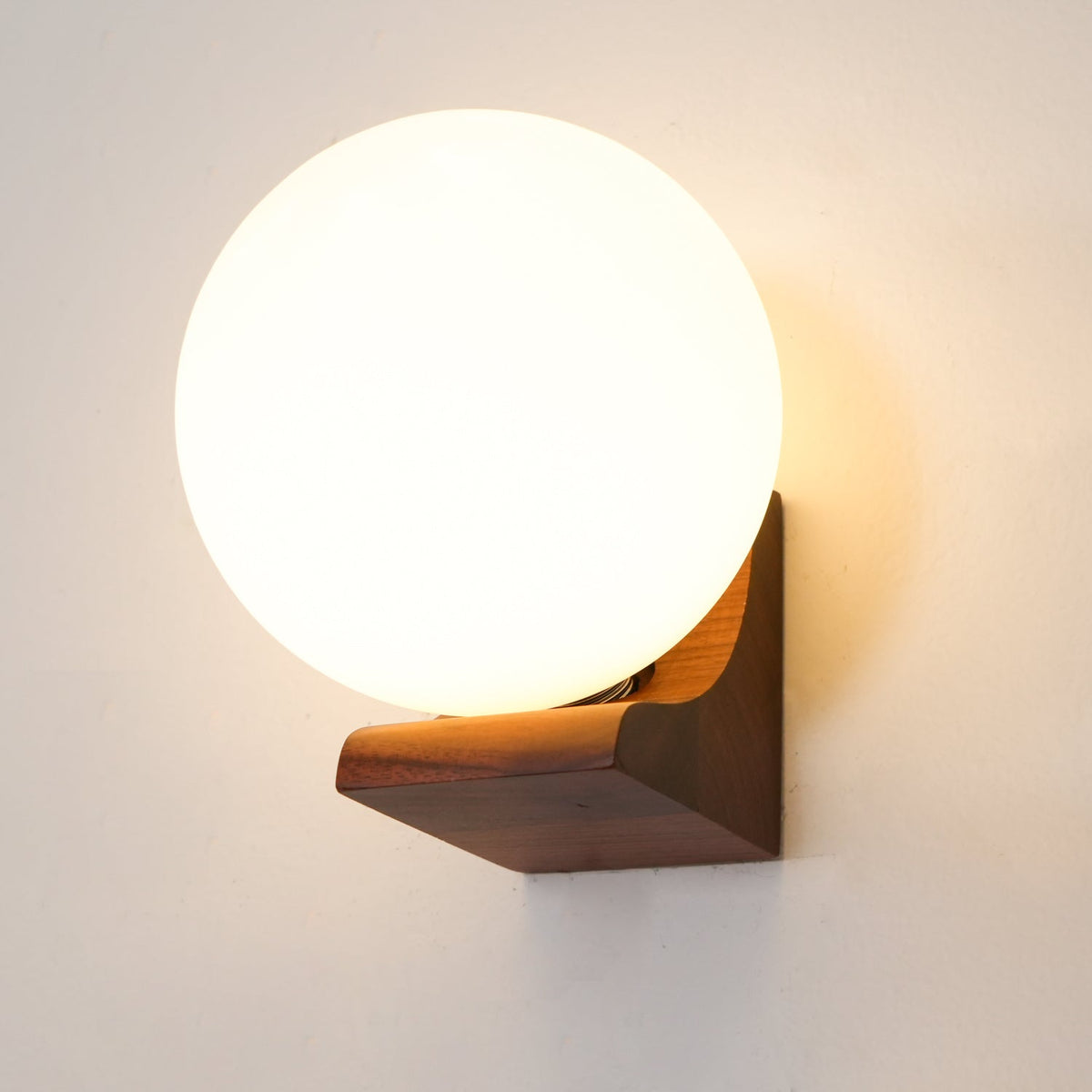 Large glowing glass globe above a walnut wooden bracket, this Clérachic wall light on a soft cream wall.