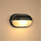 Clérachic black oval wall lamp with a hooded cap and ribbed glass lens, giving a warm glow on a textured plaster wall.