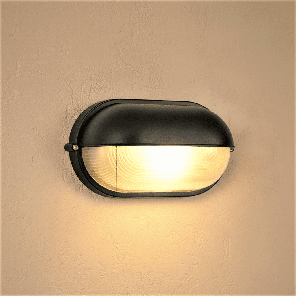 Clérachic black oval wall lamp with a hooded cap and ribbed glass lens, giving a warm glow on a textured plaster wall.