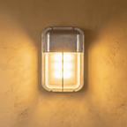 Clérachic upright rectangular wall lamp in raw galvanised metal with a ribbed glass panel, giving a warm glow on a limewash wall.
