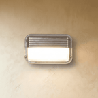 Clérachic landscape rectangular wall lamp in galvanised metal, with a ridged hood over a frosted glass panel, lit on a plaster wall.