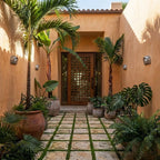 Clérachic half-dome wall lamps along terracotta courtyard walls, leading to a carved timber door among palms and potted plants.