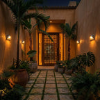 Clérachic half-dome wall lamps glowing amber at dusk along a terracotta courtyard wall, with palms and a lattice timber door.
