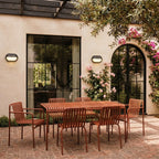 Clérachic oval wall lamps in dark housings lit beside a glazed door above a terracotta-coloured dining set and climbing roses.