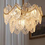 Close view of the embossed glass panels and swags of pearl beads on this lit Clérachic chandelier, with curtains behind.
