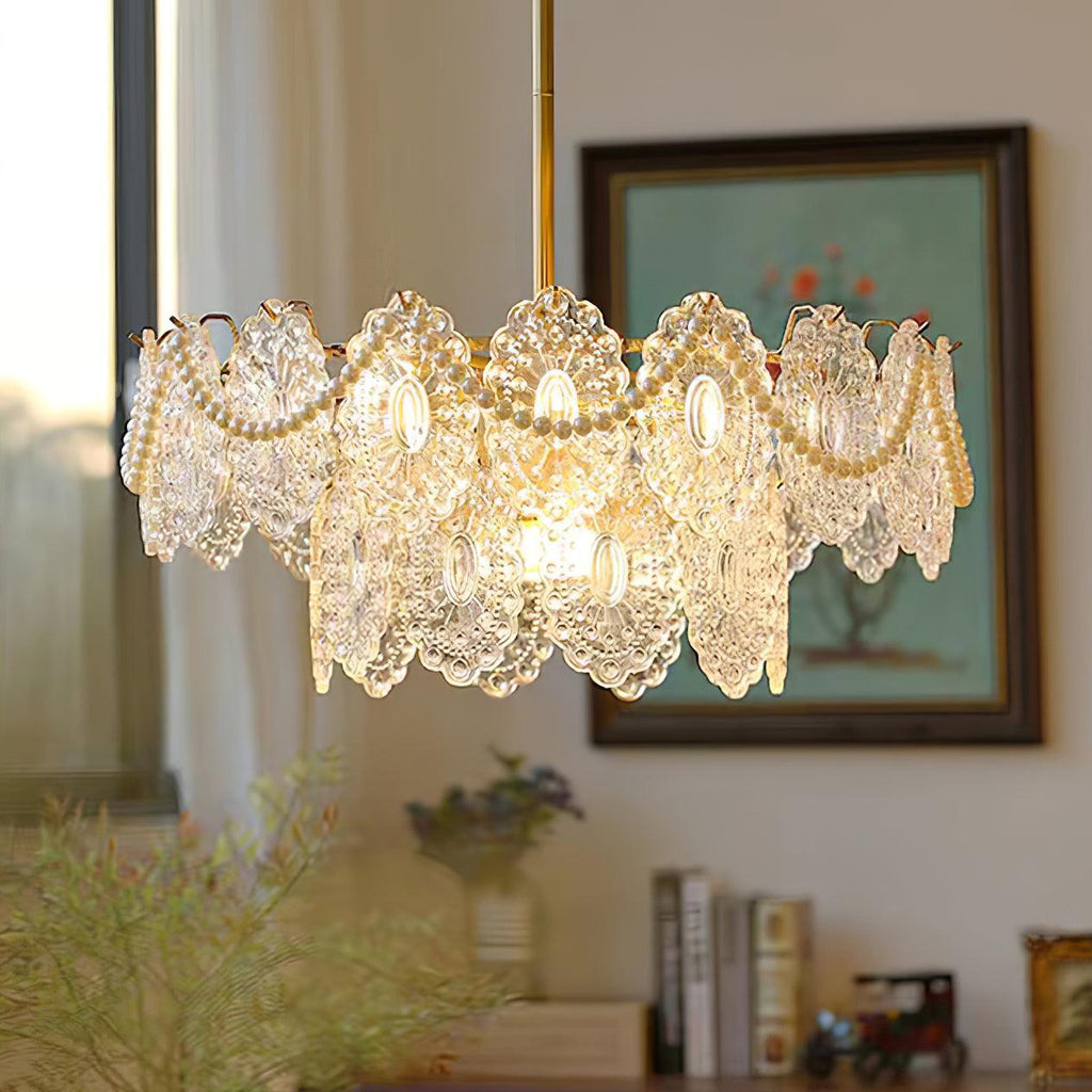 A Clérachic chandelier glowing warm above a sideboard with books, a framed picture and a leafy plant.