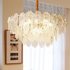 Clérachic chandelier hanging from a wrapped gold cord in front of a sheer curtain and a framed print.