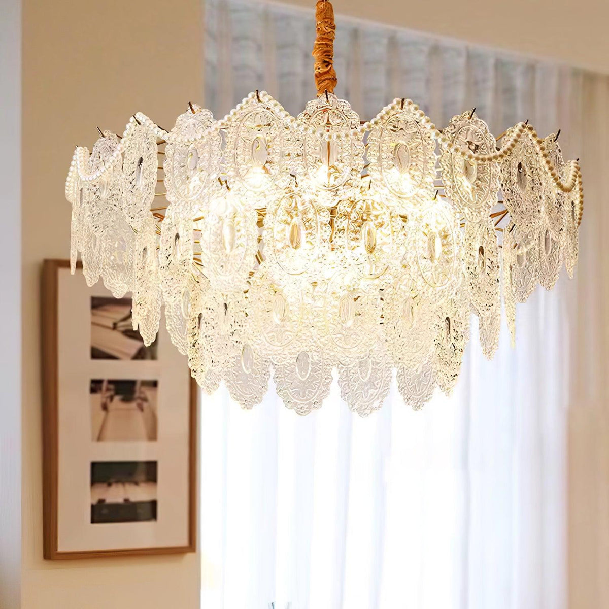 Clérachic chandelier hanging from a wrapped gold cord in front of a sheer curtain and a framed print.