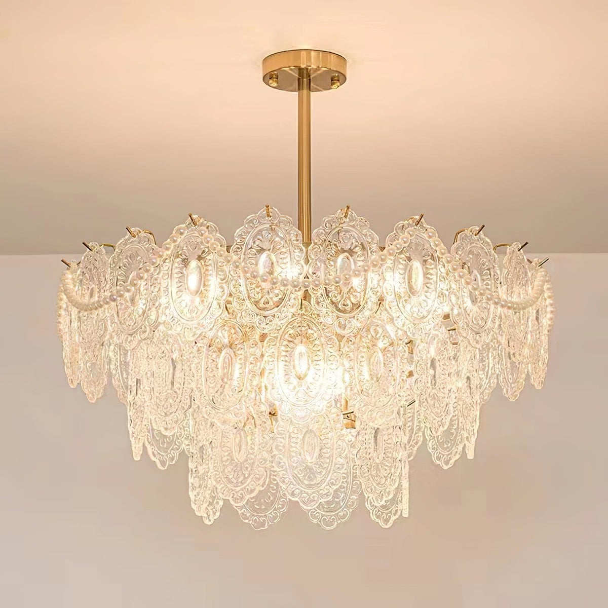Looking up at a lit Clérachic chandelier with layered glass panels and pearl strands, against a pale ceiling.