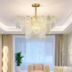 Clérachic glass chandelier lit in a living room with a moulded ceiling, a cream sofa and a tall white floor lamp.