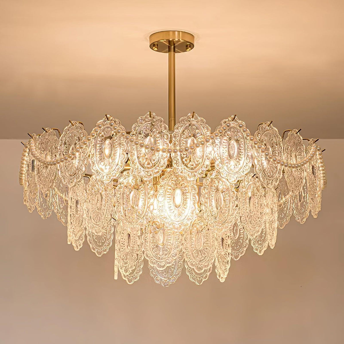 Lit Clérachic chandelier with layered patterned glass and pearl strands, hanging from a gold rod under a peach ceiling.