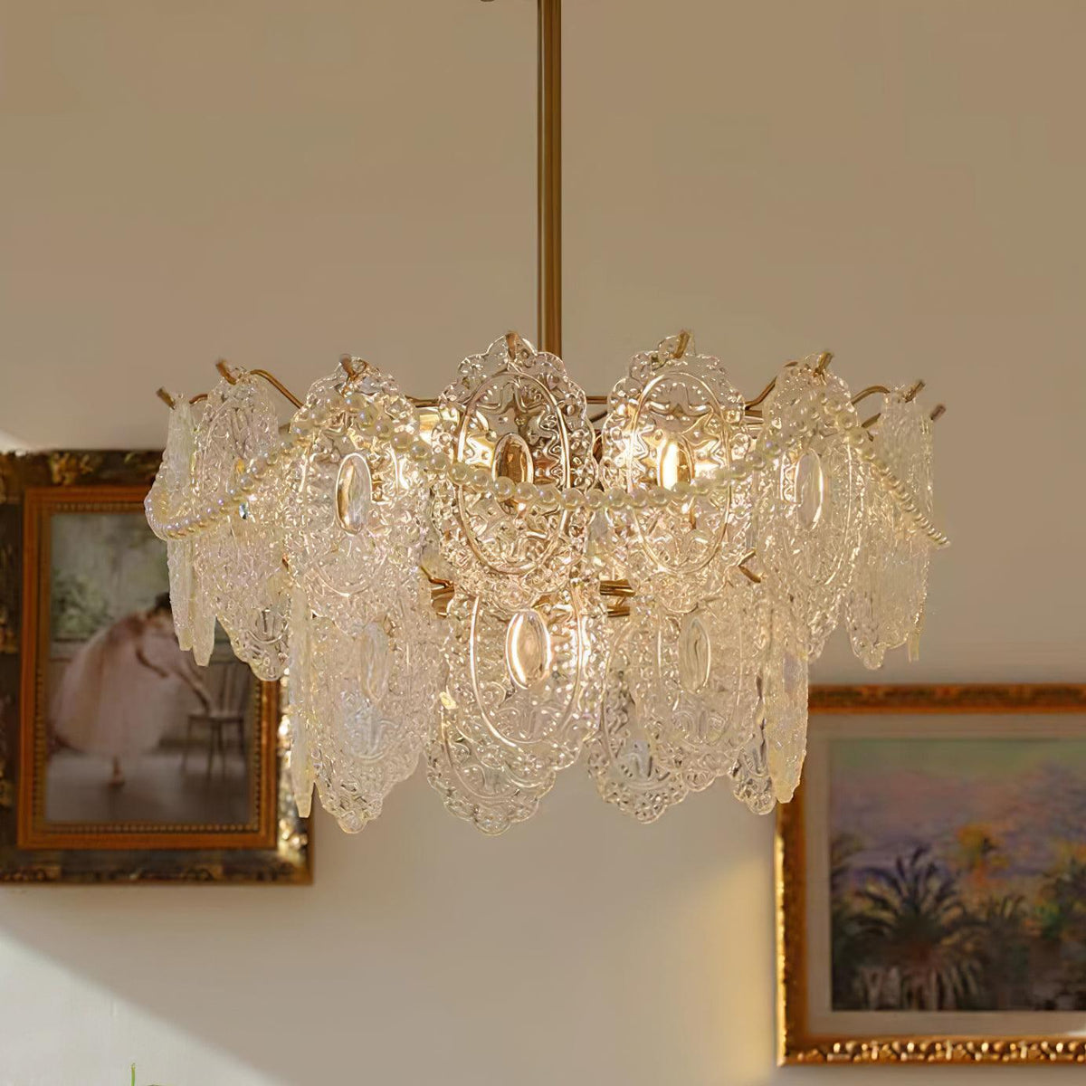 Clérachic chandelier with two rows of patterned glass panels and pearl swags, beside two framed paintings.