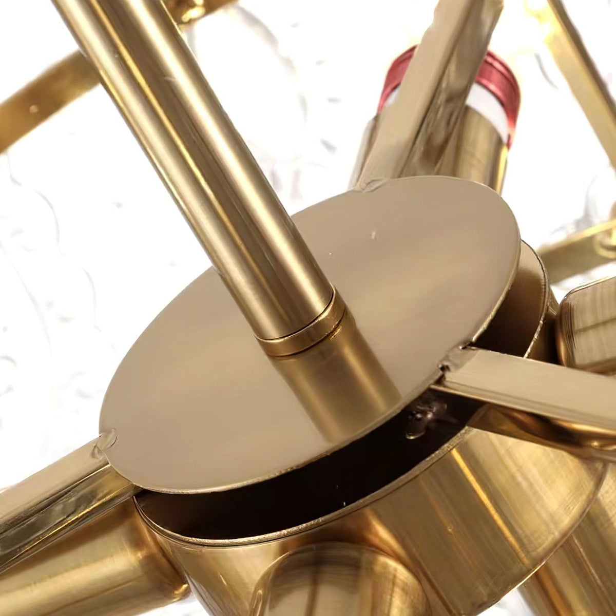 Underside detail of the gold hub and metal arms inside this Clérachic chandelier, with the lamp holders around it.
