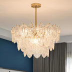 Lit Clérachic glass chandelier with several layers of clear patterned panels, against a deep blue wall and grey curtain.
