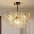 A Clérachic chandelier with pearl swags across its upper glass tier, glowing warm below a bronze-toned ceiling plate.