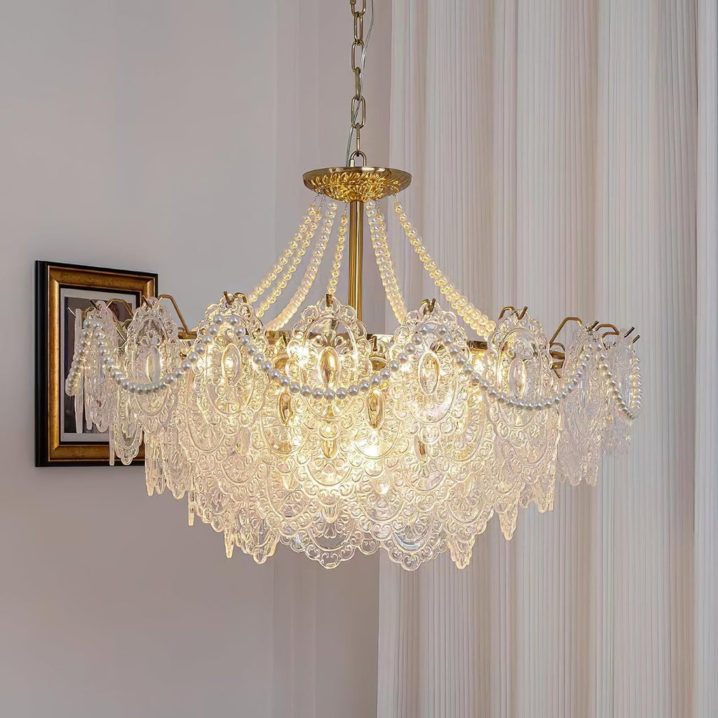 Lit Clérachic pendant with lace-patterned glass panels and pearl swags, hanging beside a framed portrait and a pleated sheer curtain.