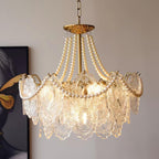 Close angle on the lit Clérachic pendant, with pearl strands looping over embossed glass panels and a gold canopy above on a beige wall.