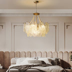 A lit Clérachic pendant with pearl swags and embossed glass hangs in a bedroom with a padded blush headboard and panelled walls.