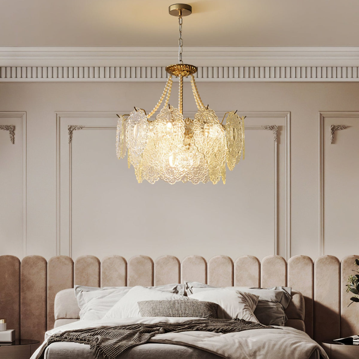 A lit Clérachic pendant with pearl swags and embossed glass hangs in a bedroom with a padded blush headboard and panelled walls.