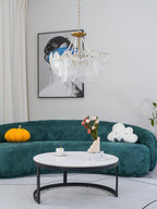 Clérachic pendant light with pearl-draped glass panels in a living room with a curved green velvet sofa and a round white marble coffee table.