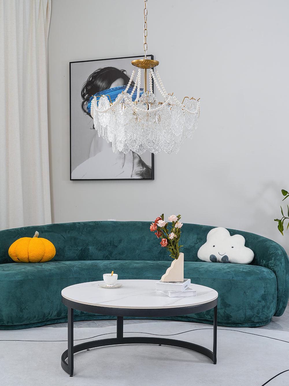 Clérachic pendant light with pearl-draped glass panels in a living room with a curved green velvet sofa and a round white marble coffee table.