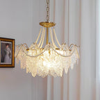 Lit Clérachic pendant with embossed glass panels and pearl strands on a gold stem, beside a gilt-framed portrait and a pleated curtain.