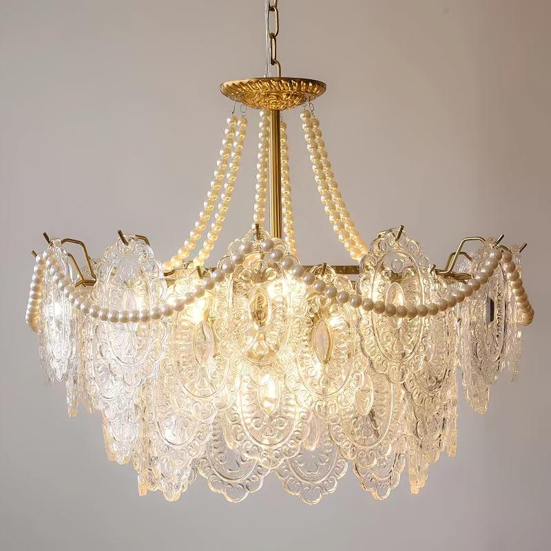 Close view of the Clérachic pendant's gold canopy, pearl strands and layered clear glass panels, lit against a plain beige wall.